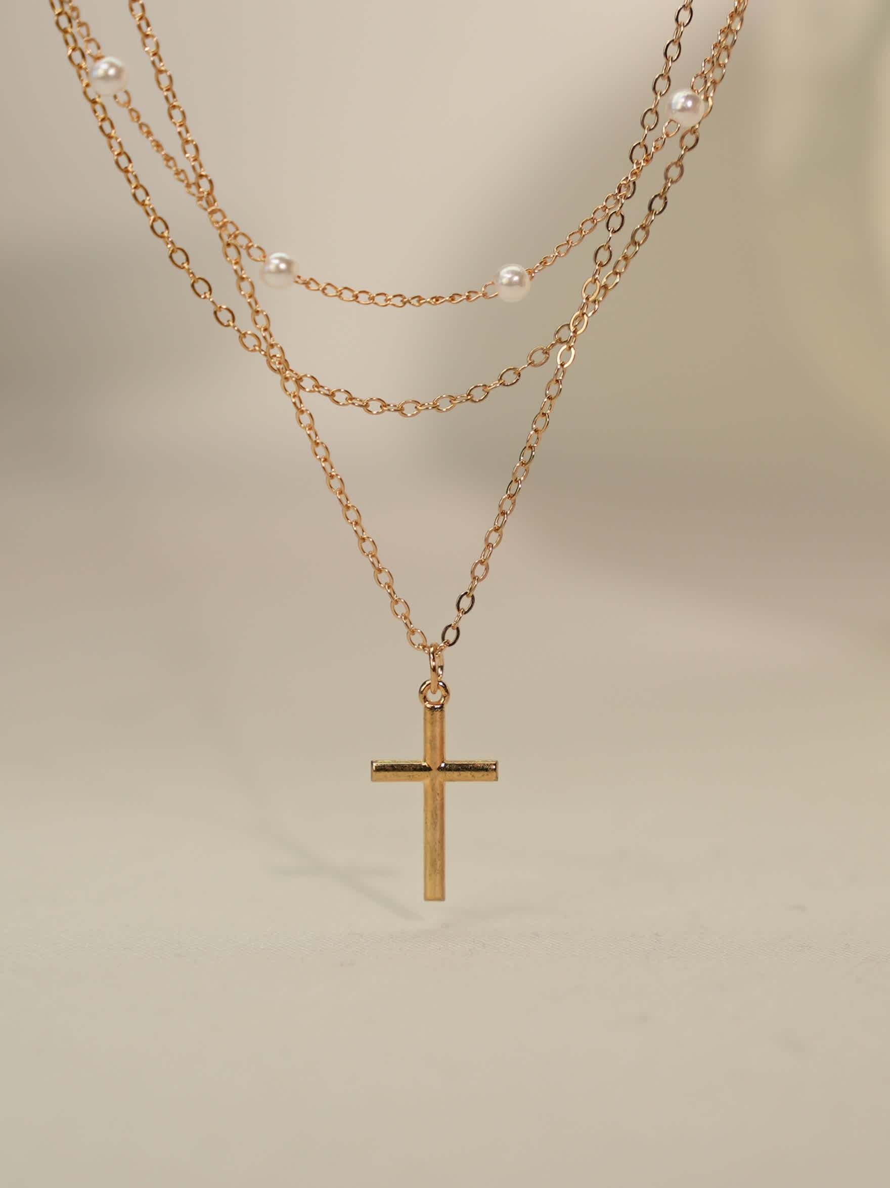 Minimalist pearl and cross necklace photographed on neutral stone backdrop