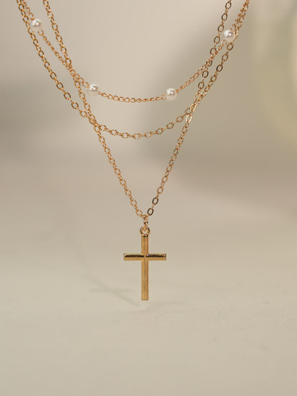 Minimalist pearl and cross necklace photographed on neutral stone backdrop