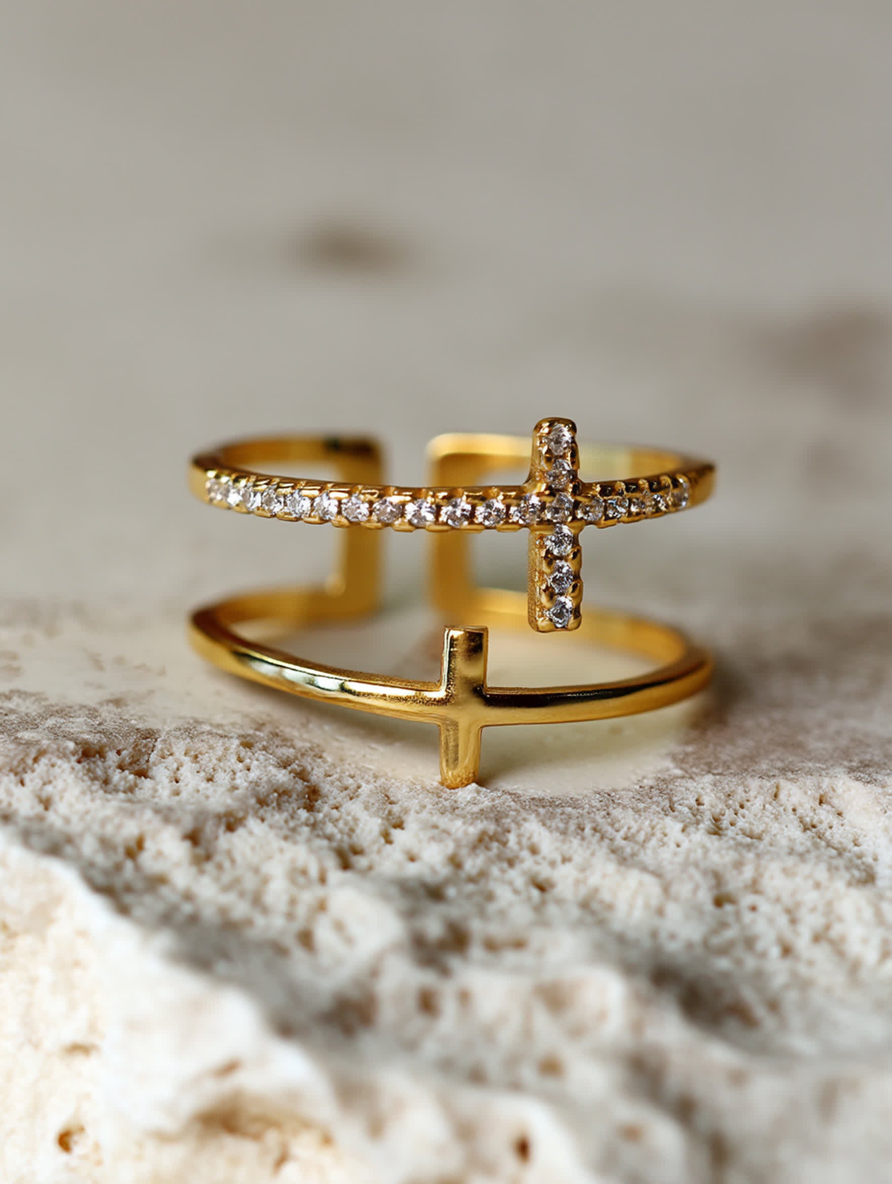 Minimalist photo of the double cross ring against a soft white fabric background, emphasizing the polished 18K gold tone and delicate craftsmanship