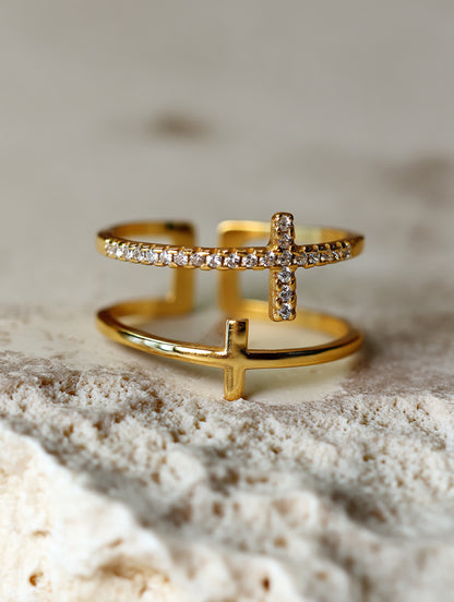 Minimalist photo of the double cross ring against a soft white fabric background, emphasizing the polished 18K gold tone and delicate craftsmanship