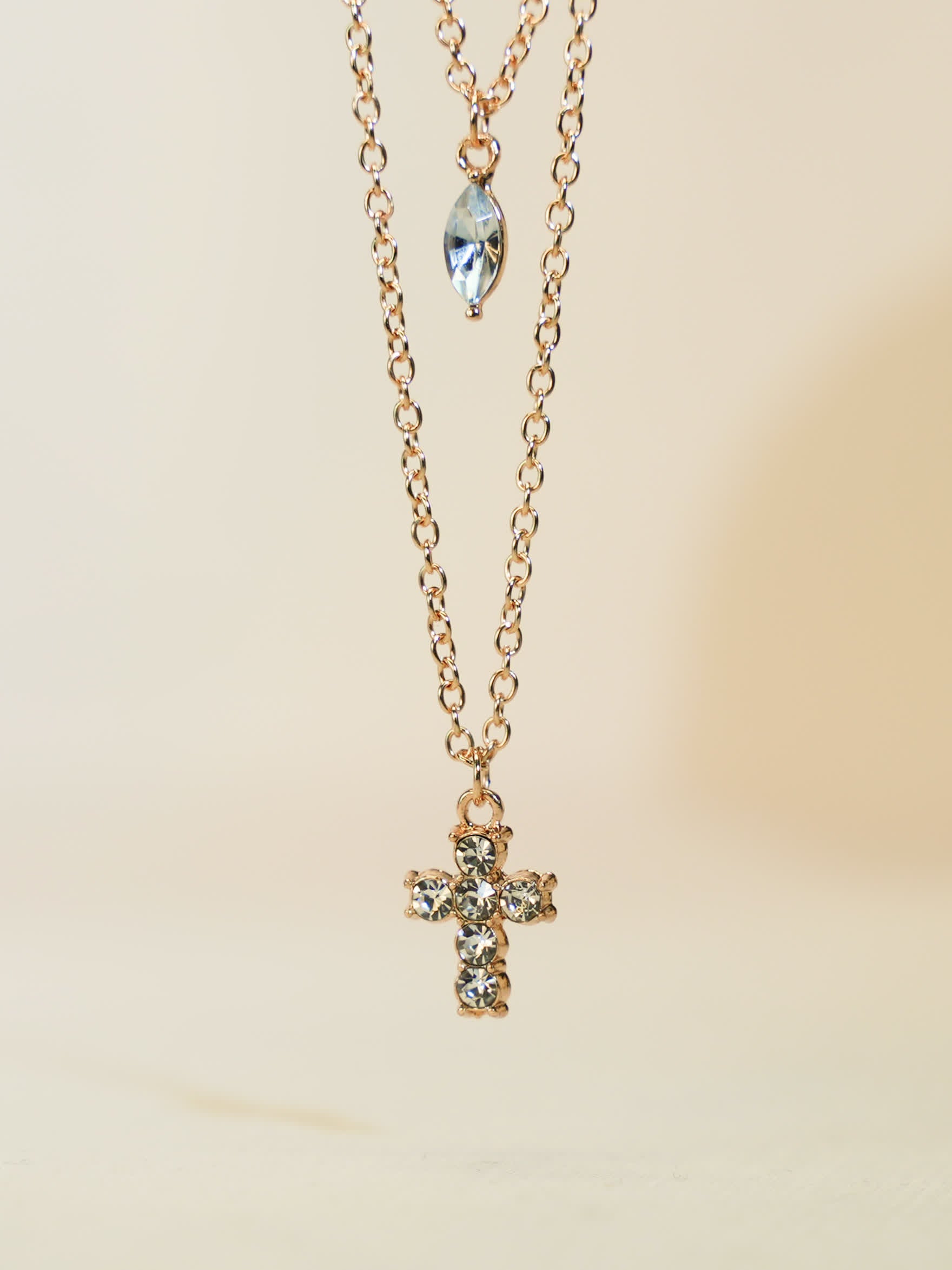Minimalist product photo of layered gold cross necklace standing upright against clean ivory surface