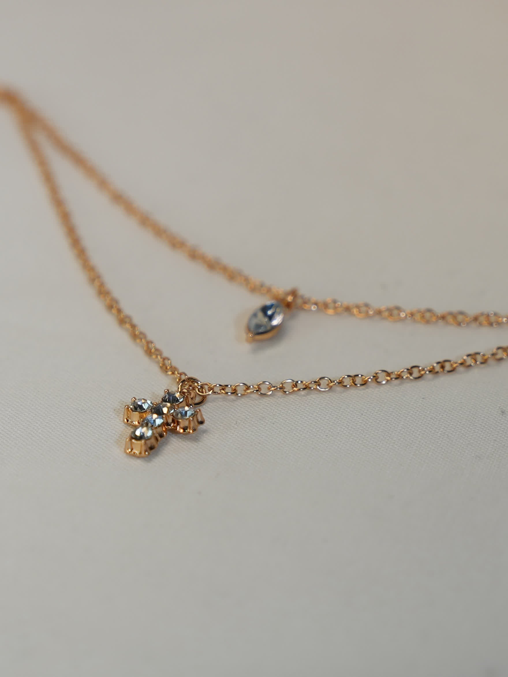 Close-up shot of double chain necklace laid flat showing fine detailing of marquise and pavé cross pendants