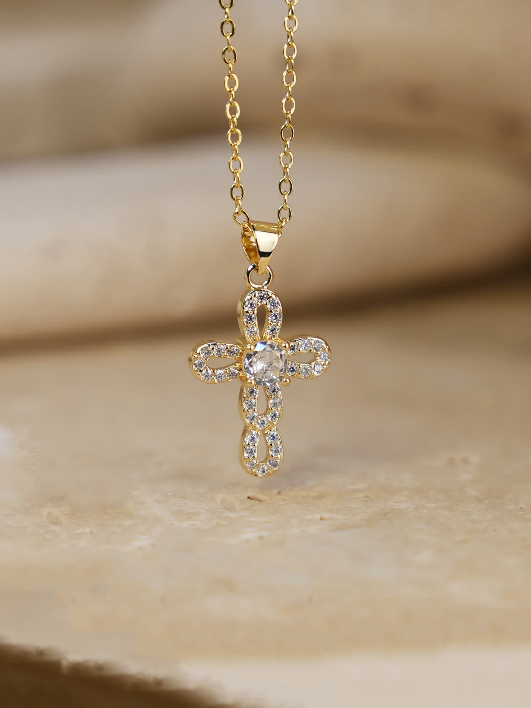 Close-up of loop cross necklace resting on beige travertine slab, showcasing crystal detail