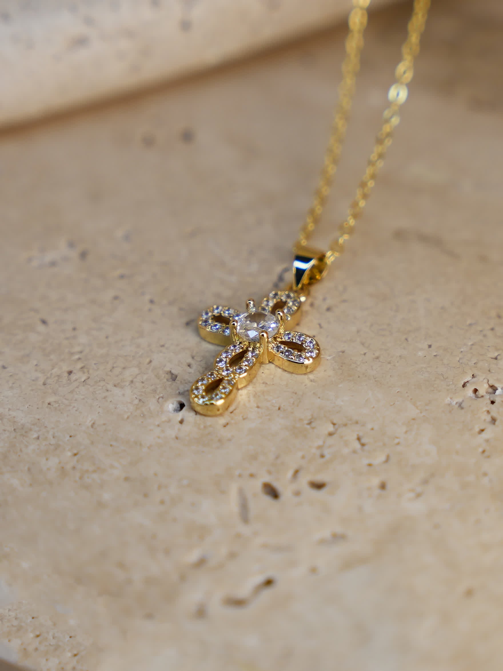 Side angle of gold loop cross pendant laying flat on stone, highlighting interlocking design
