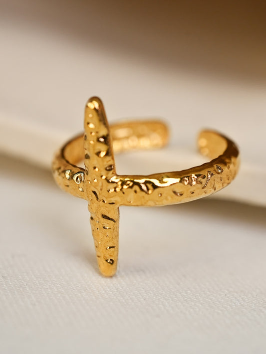 Chunky gold open cross ring resting on fabric surface