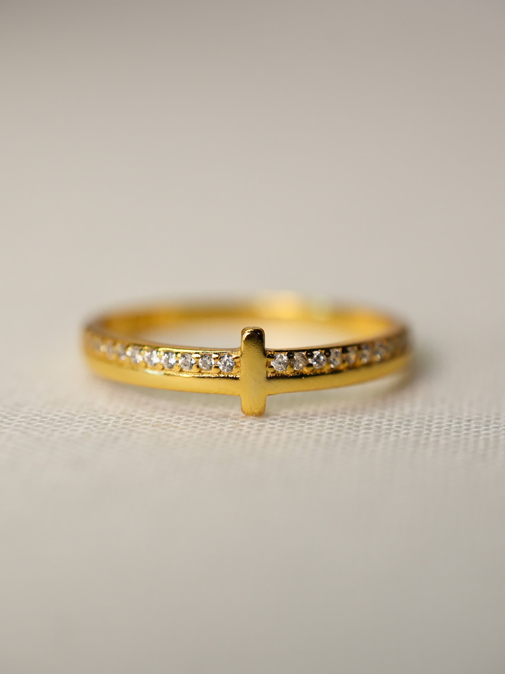 Elegant gold cross ring displayed flat with sparkling stone band