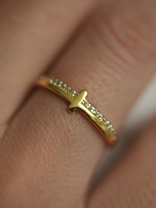 Dainty gold cross ring worn on finger with natural lighting