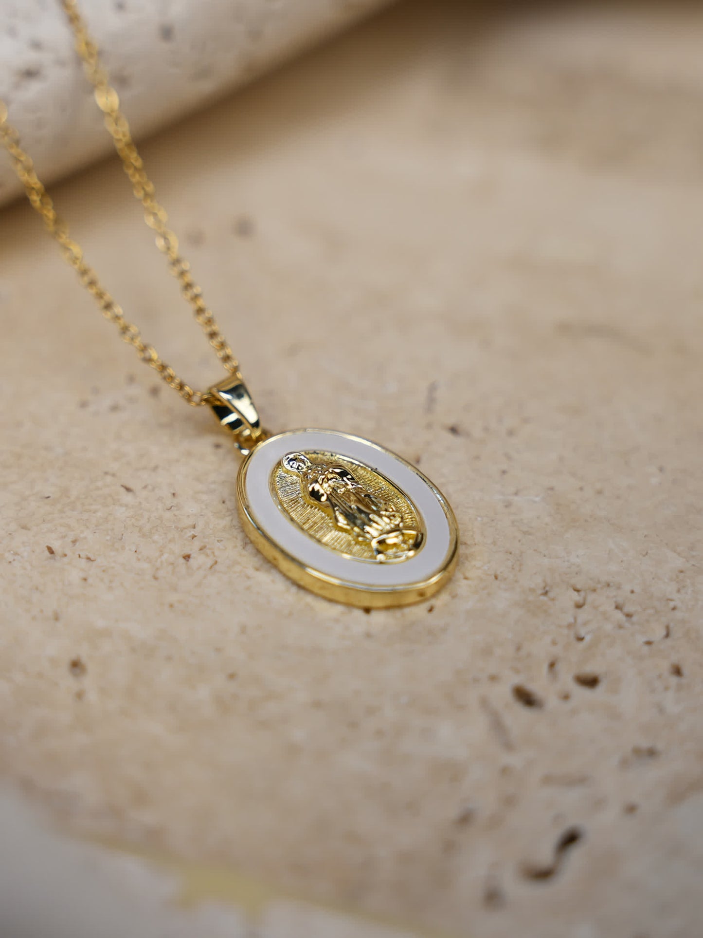 Elegant lifestyle photo of the Madonna necklace laid on stone showing the engraved Virgin Mary design and radiant gold tones with a delicate chain.