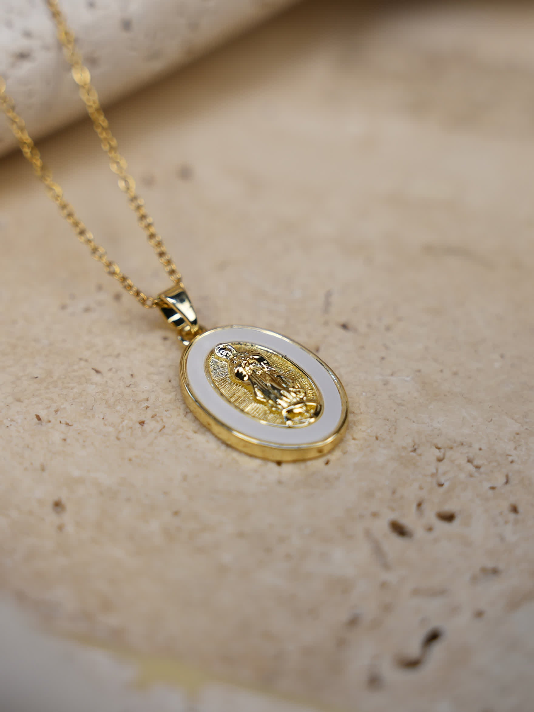 Elegant lifestyle photo of the Madonna necklace laid on stone showing the engraved Virgin Mary design and radiant gold tones with a delicate chain.