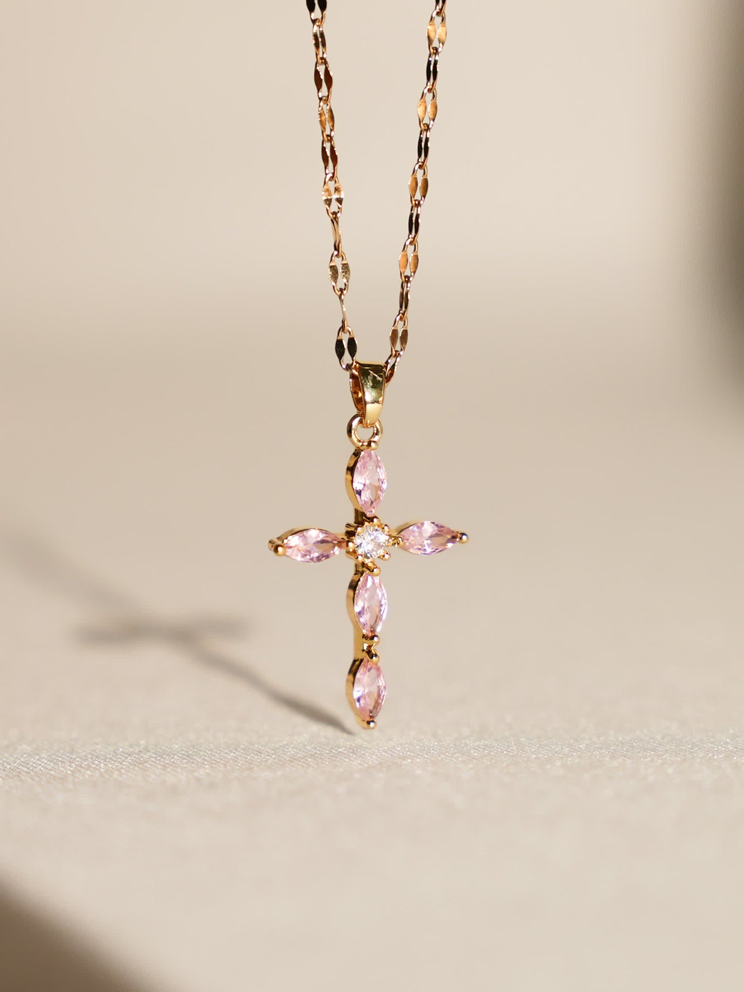Pink crystal cross necklace displayed upright on soft neutral background with gentle lighting