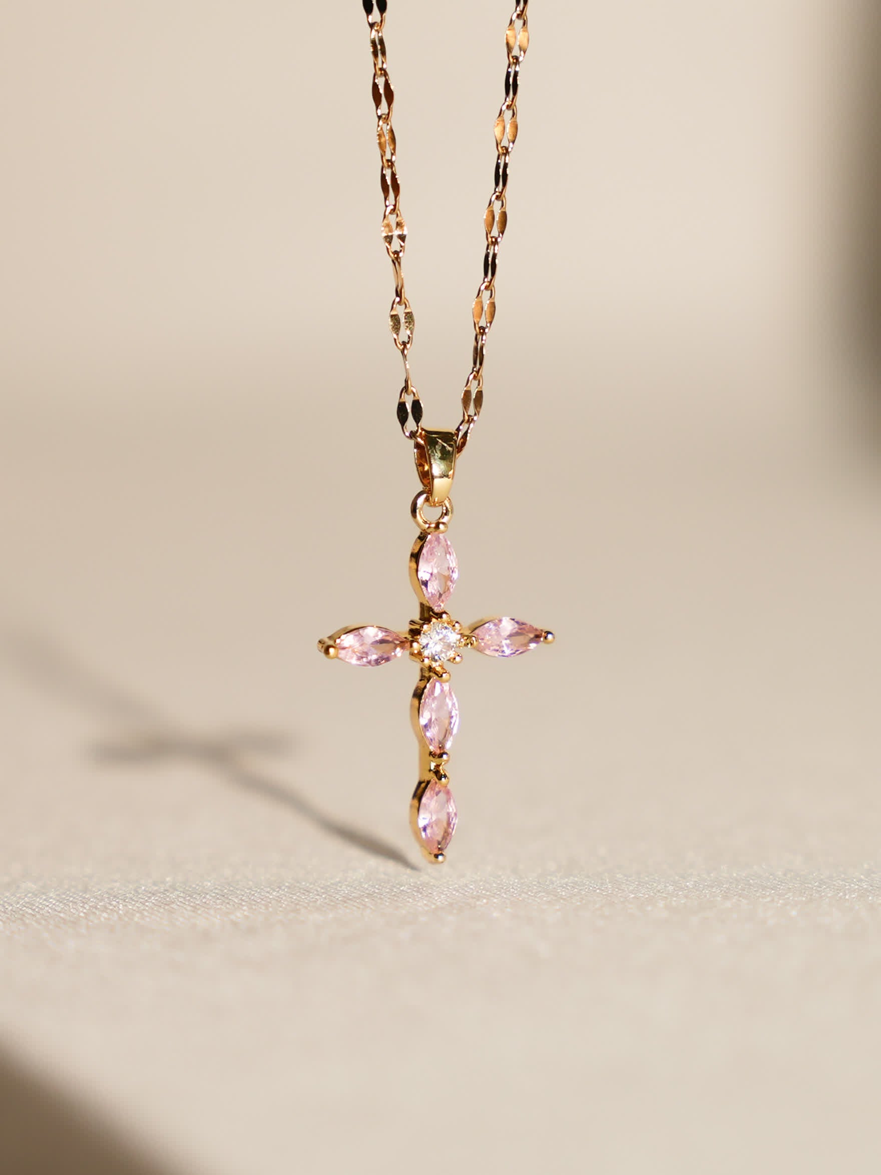 Pink crystal cross necklace displayed upright on soft neutral background with gentle lighting
