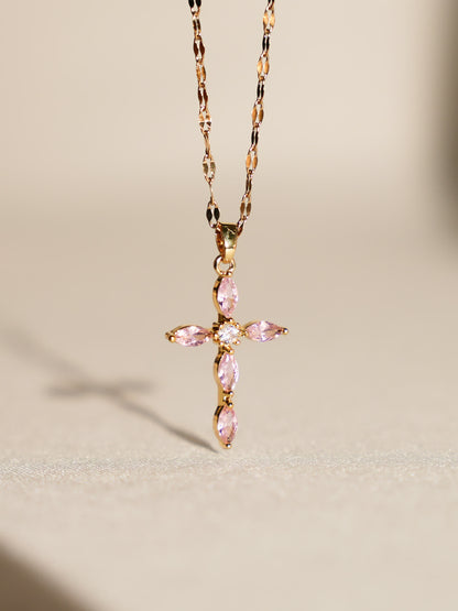 Pink crystal cross necklace displayed upright on soft neutral background with gentle lighting