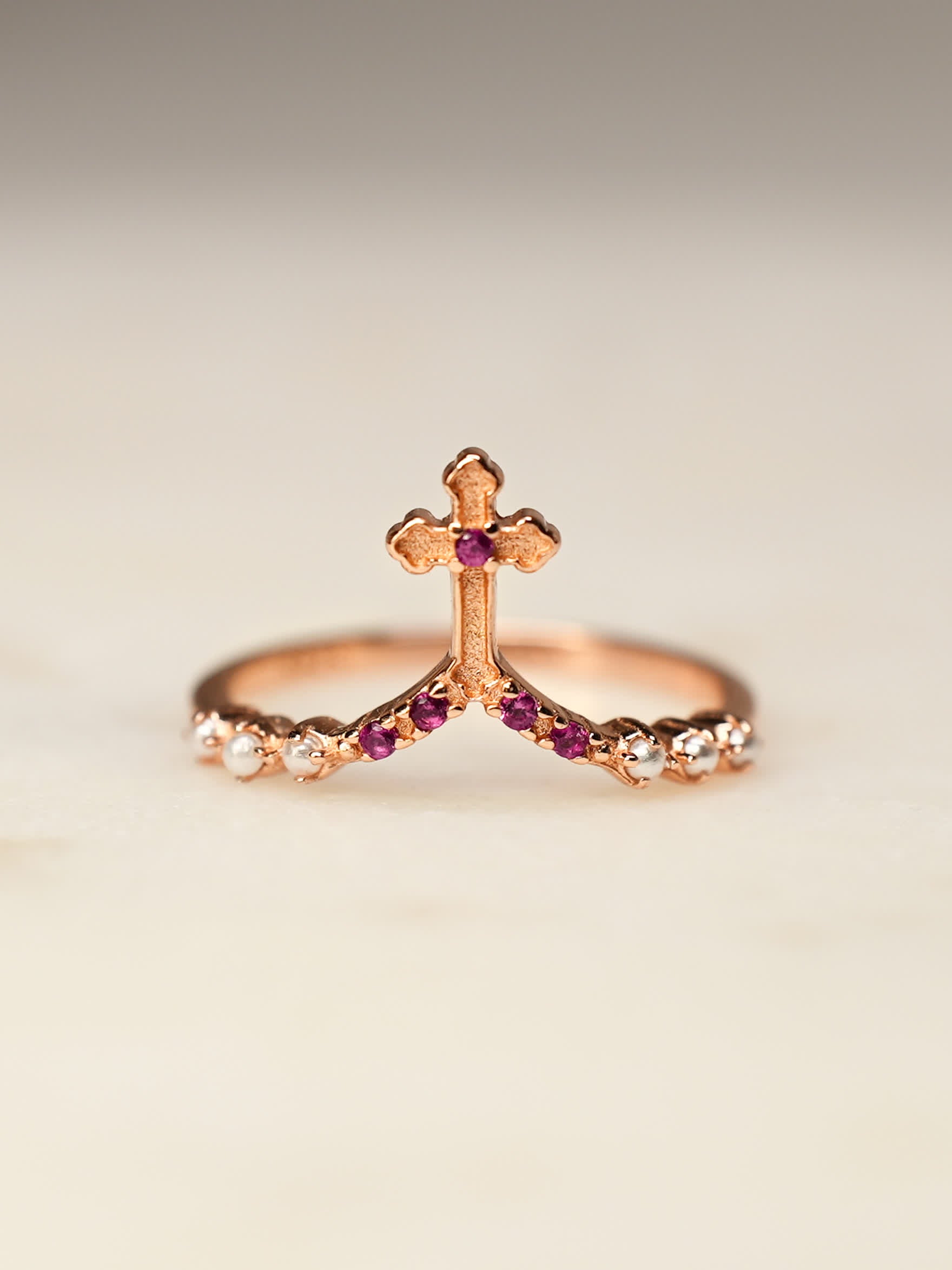 Close-up of rose gold ring with cross and cubic zirconias on cream stone surface