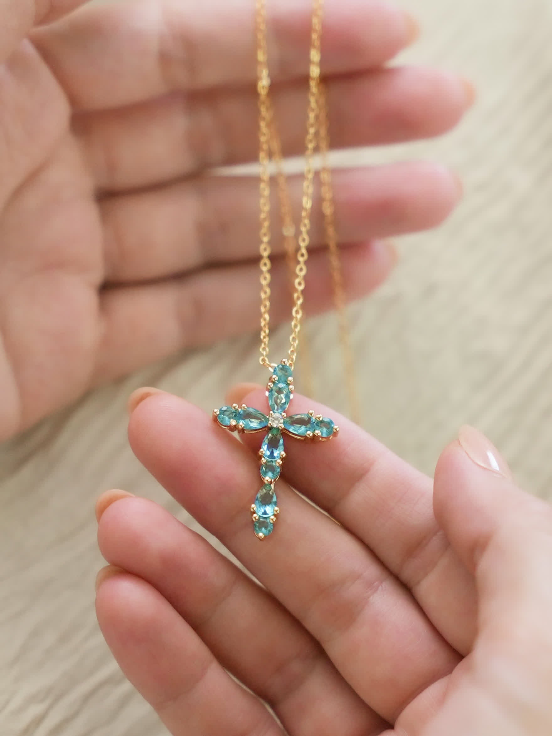 Hand holding the feminine cross pendant, showcasing scale, crystal details, and soft shine