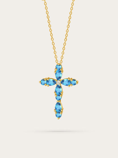 Studio photo of feminine cross pendant with aquamarine zircon stones set in gold, displayed on soft beige background