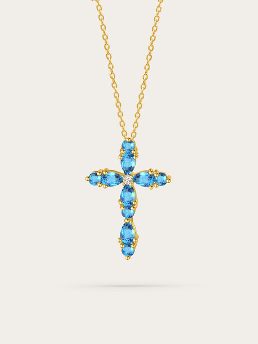 Studio photo of feminine cross pendant with aquamarine zircon stones set in gold, displayed on soft beige background