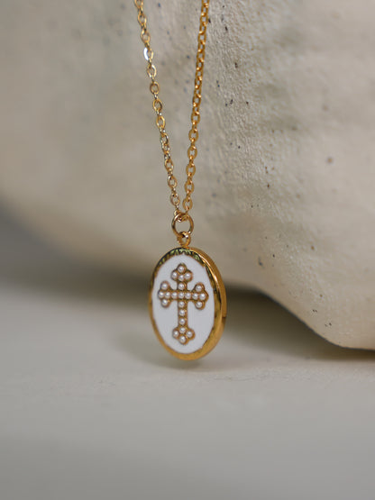 Pendant leaning on light stone texture
Close-up of gold and white enamel cross necklace draped over curved stone