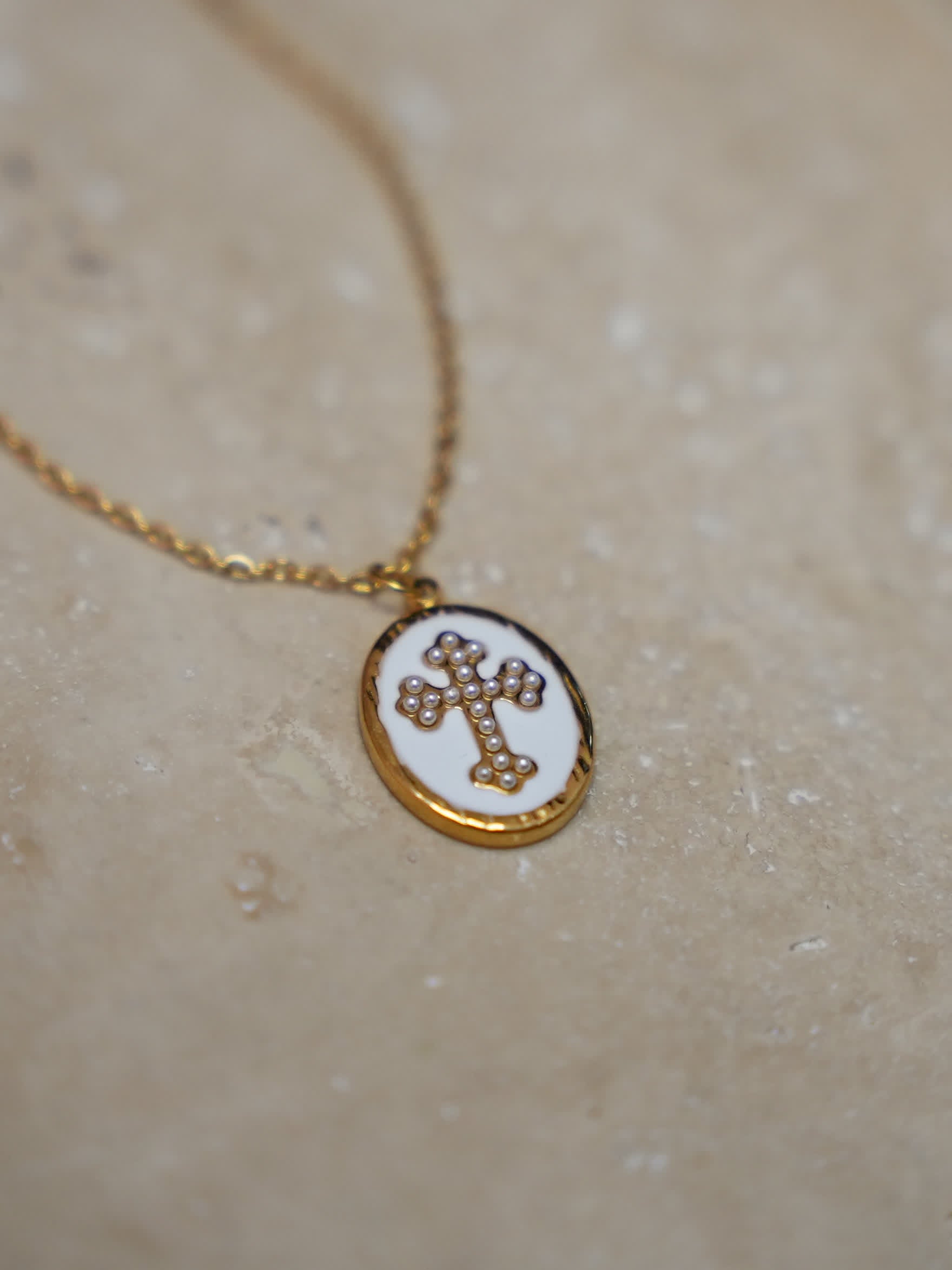 Pendant on warm stone surface
Enamel cross necklace with gold oval pendant resting on natural stone