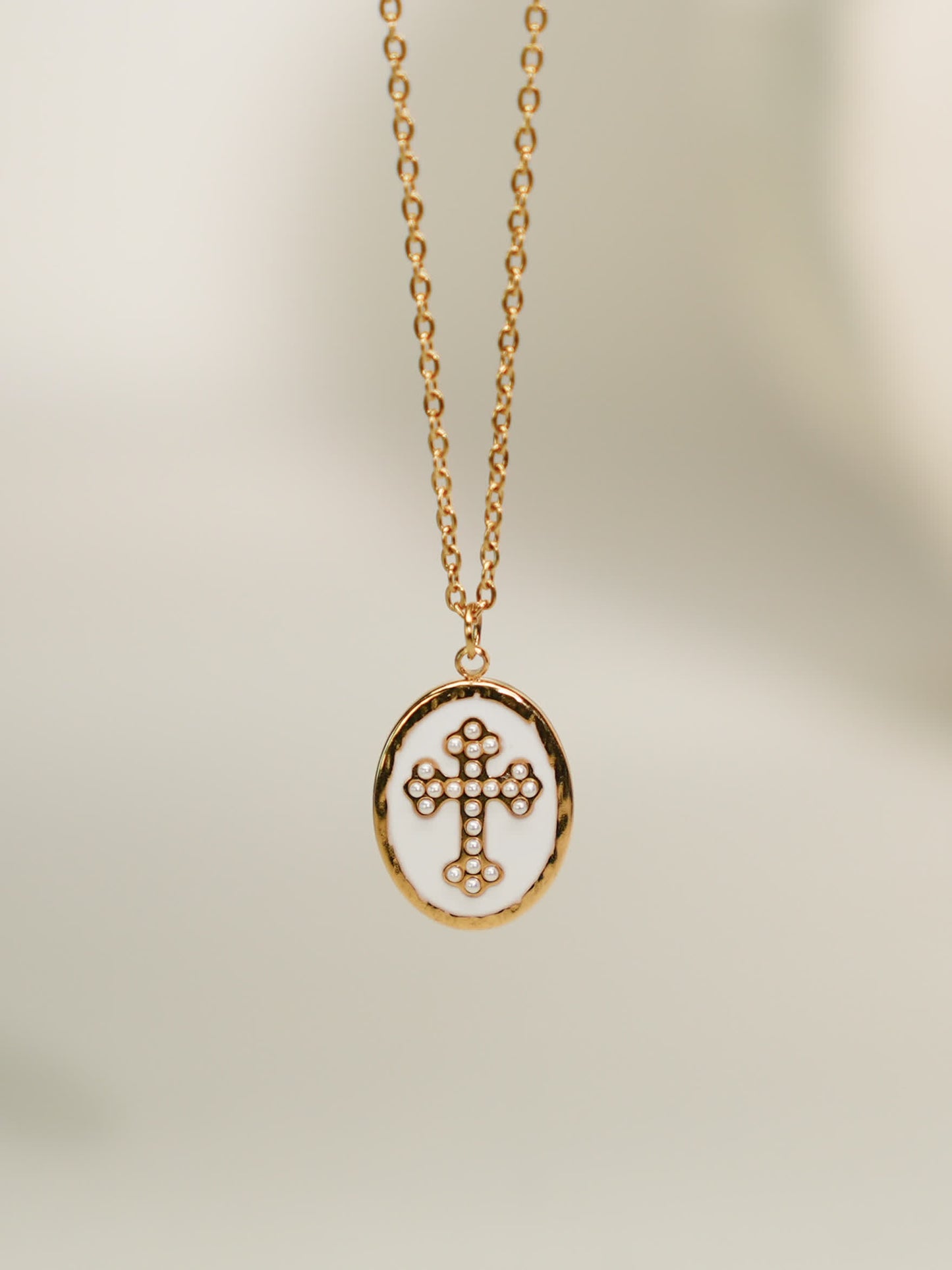 Front-facing necklace on soft background
Gold enamel cross necklace with pearl-dotted cross pendant on light beige background
