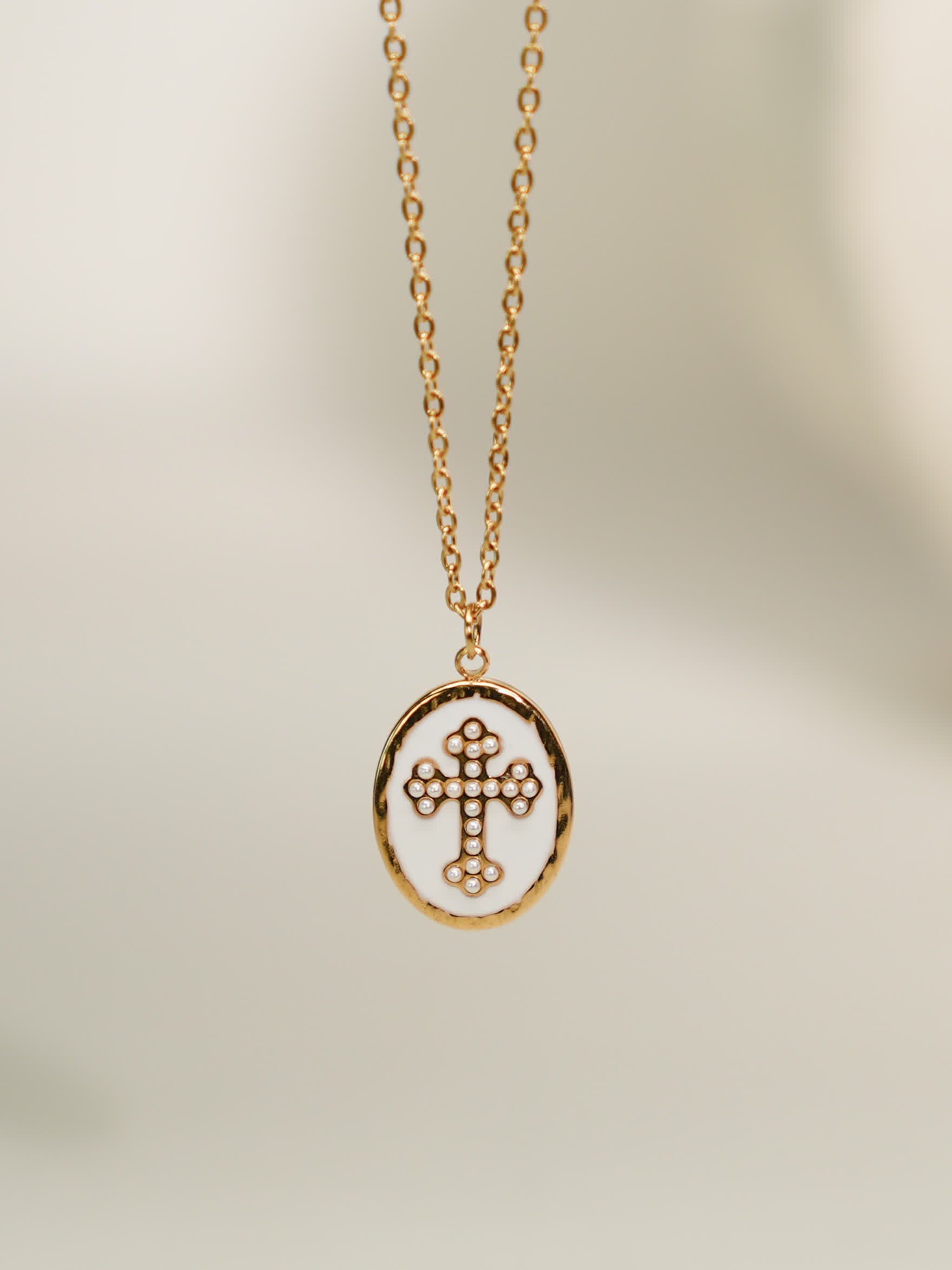 Front-facing necklace on soft background
Gold enamel cross necklace with pearl-dotted cross pendant on light beige background