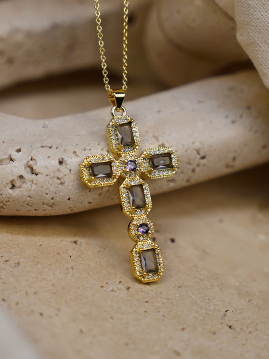 Close-up of the Faithstone Vintage Zircon Cross Necklace resting on textured stone surface, showcasing gold finish and deep-toned zircon crystals