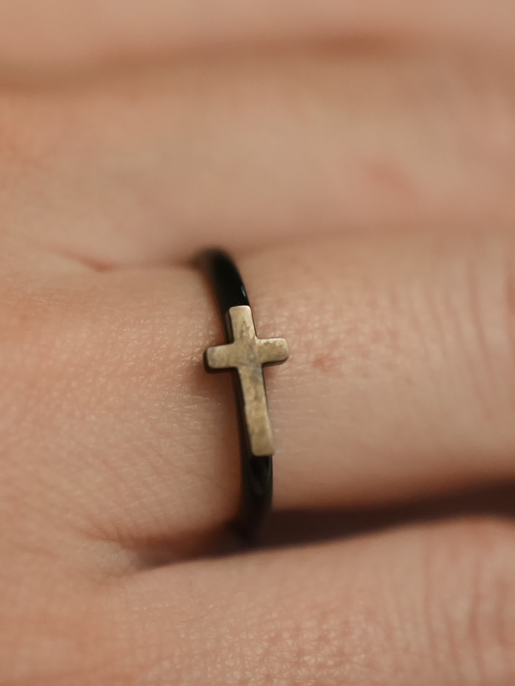 Close-up of the woman’s ring on a finger, showing the slim black band with a raised metallic cross symbol at the center.
