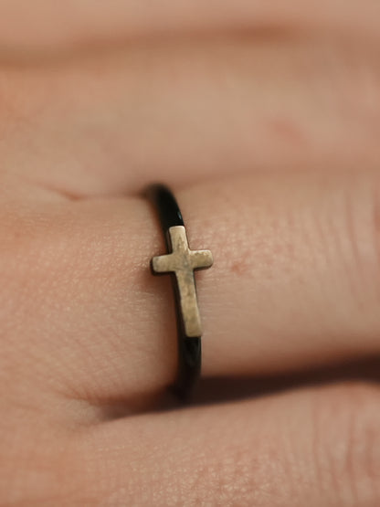 Close-up of the woman’s ring on a finger, showing the slim black band with a raised metallic cross symbol at the center.