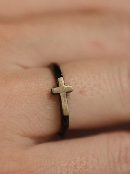 Close-up of the woman’s ring on a finger, showing the slim black band with a raised metallic cross symbol at the center.