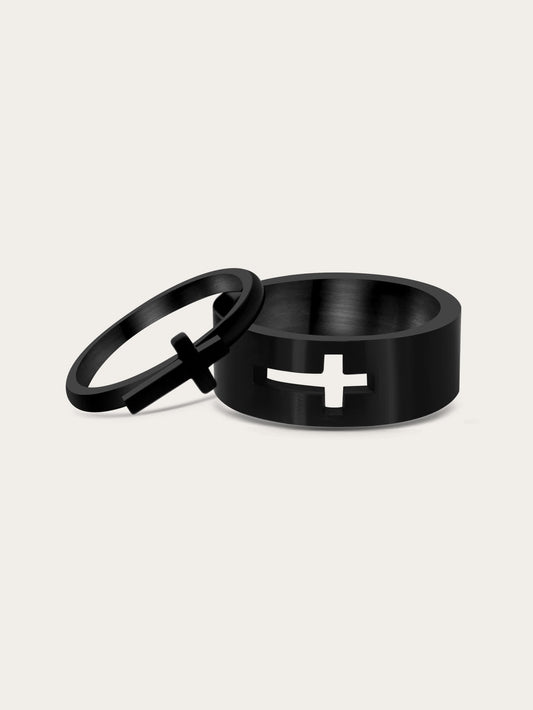 Front-facing studio image of a black stainless steel couple ring set featuring an interlocking cross design — one ring with a raised silver cross and the other with a cross-shaped cut-out.