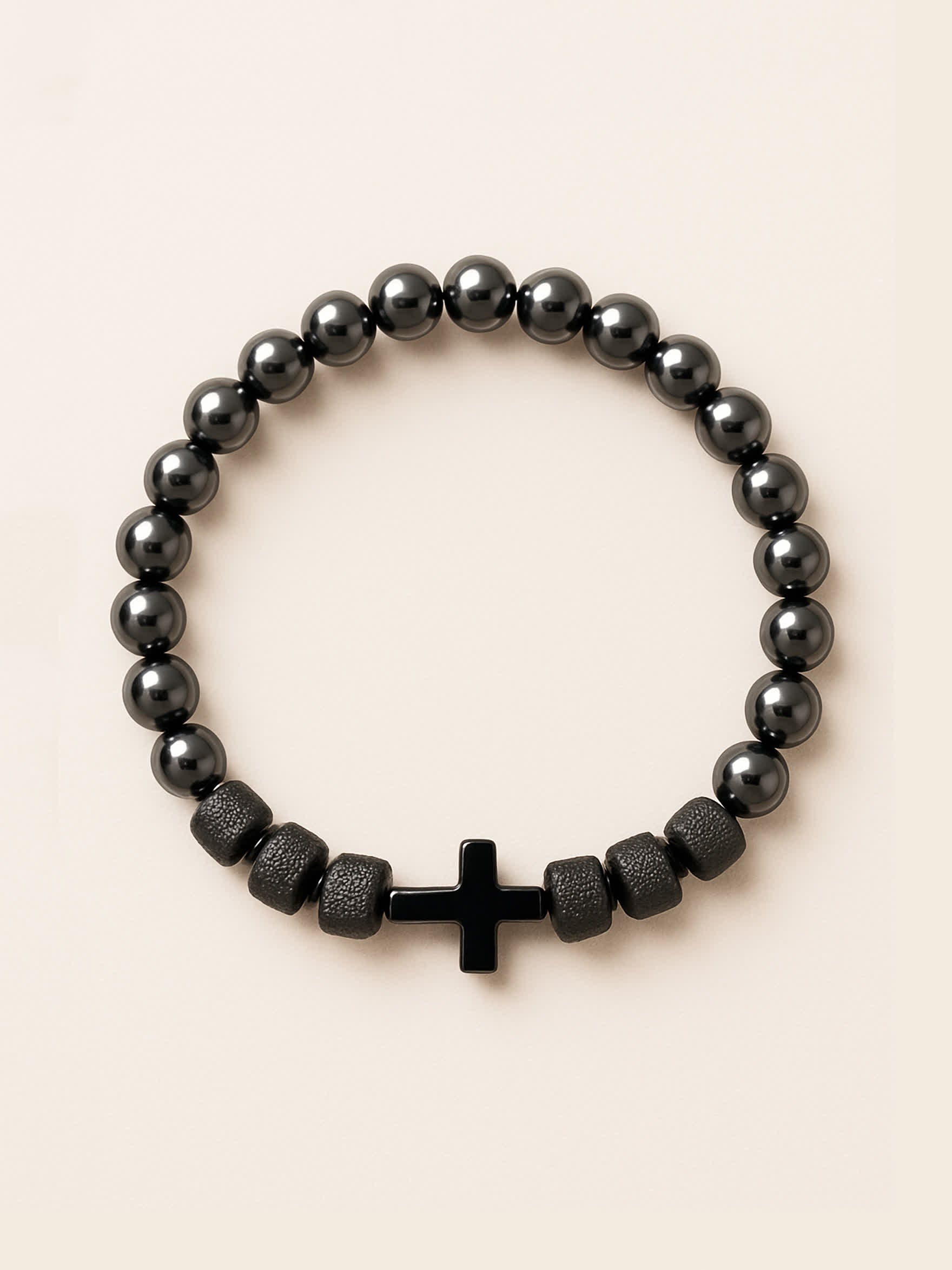 Studio image of the Iron Grace Beaded Cross Bracelet featuring glossy hematite-style gemstone beads and a centered black cross, displayed against a soft beige background.