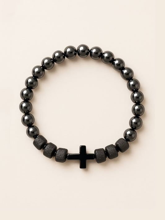 Studio image of the Iron Grace Beaded Cross Bracelet featuring glossy hematite-style gemstone beads and a centered black cross, displayed against a soft beige background.