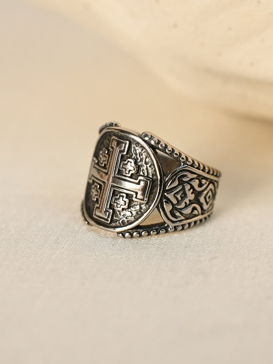 Angled studio shot of the Jerusalem cross ring placed on a soft beige surface, highlighting engraved details

