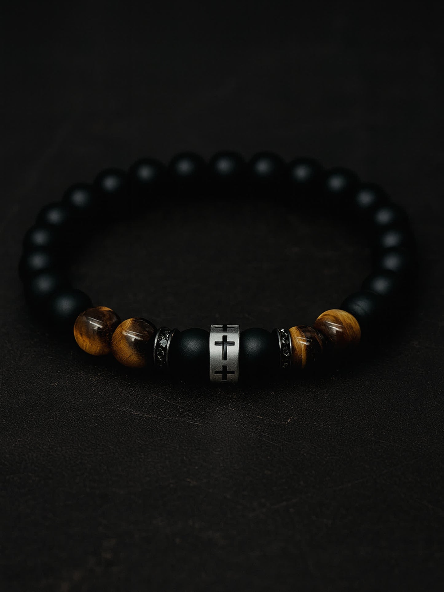 Moody overhead photo of the Lion's Peace Men's Religious Bracelet on a dark textured background, highlighting the contrast between the matte obsidian and the gleaming tiger’s eye.