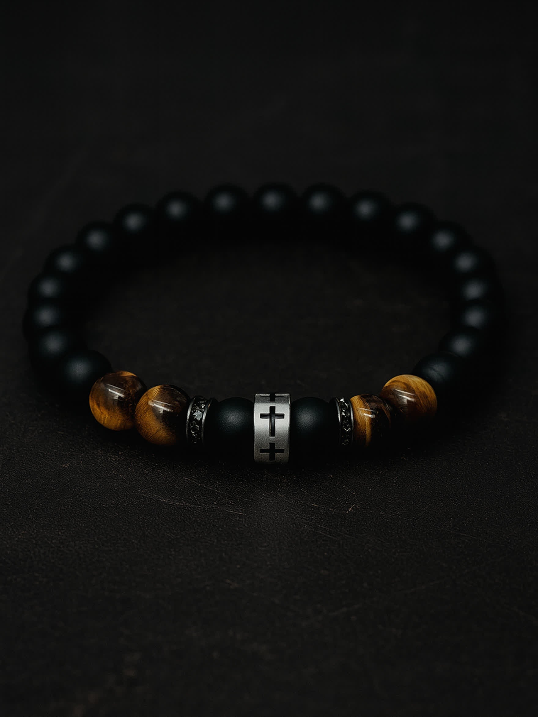 Moody overhead photo of the Lion's Peace Men's Religious Bracelet on a dark textured background, highlighting the contrast between the matte obsidian and the gleaming tiger’s eye.