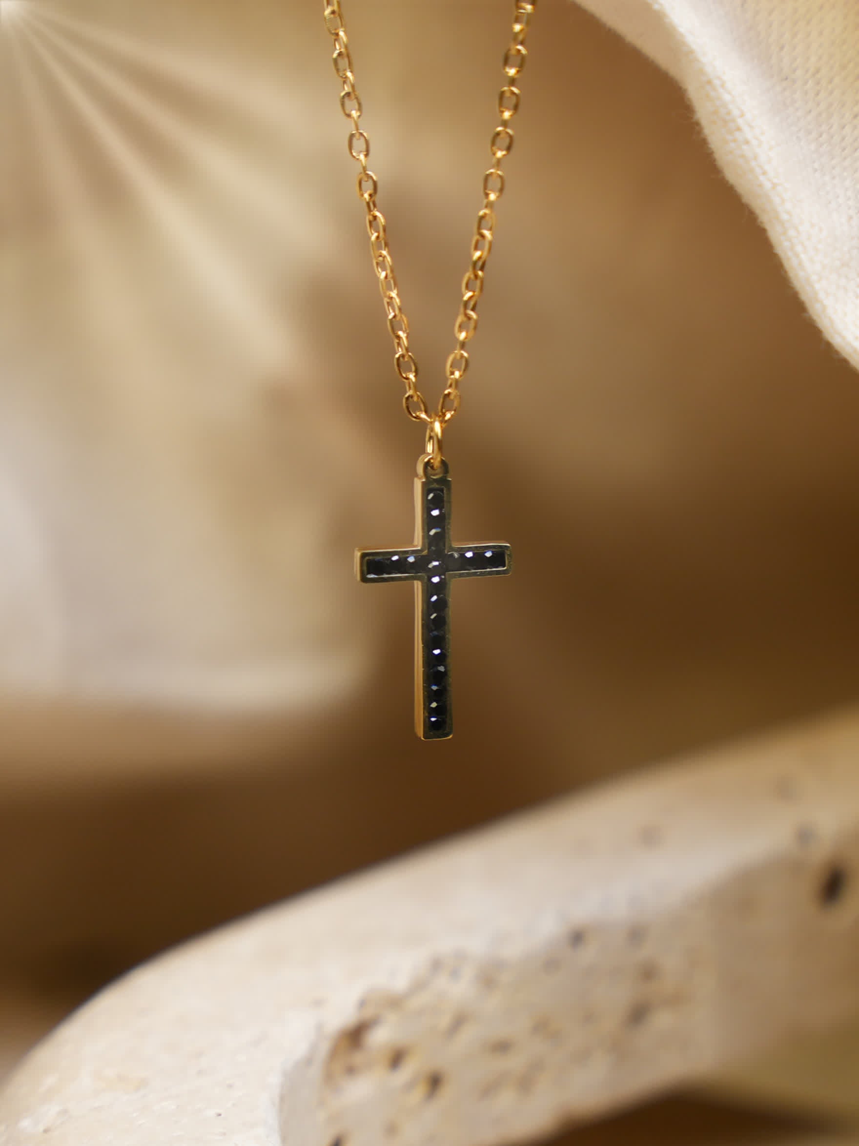Close-up of black and gold cross necklace hanging over curved beige stone