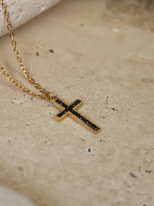 Black zircon cross pendant resting on natural travertine surface