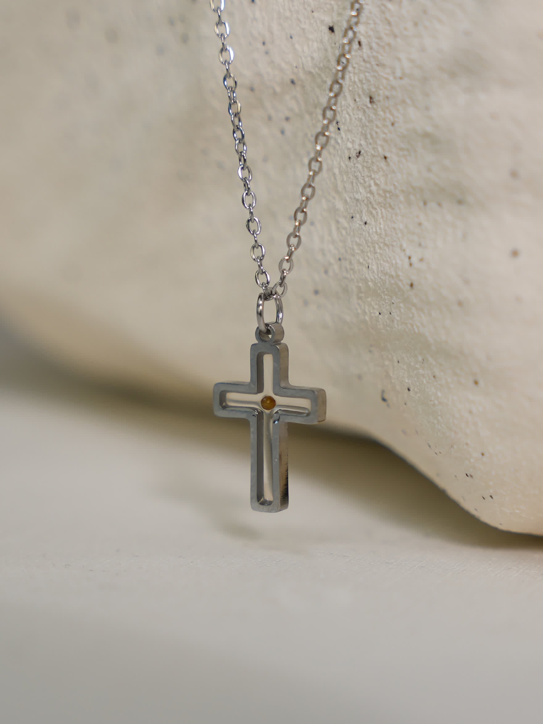 Close-up of necklace on textured stone
Silver mustard seed cross necklace resting on smooth white stone surface