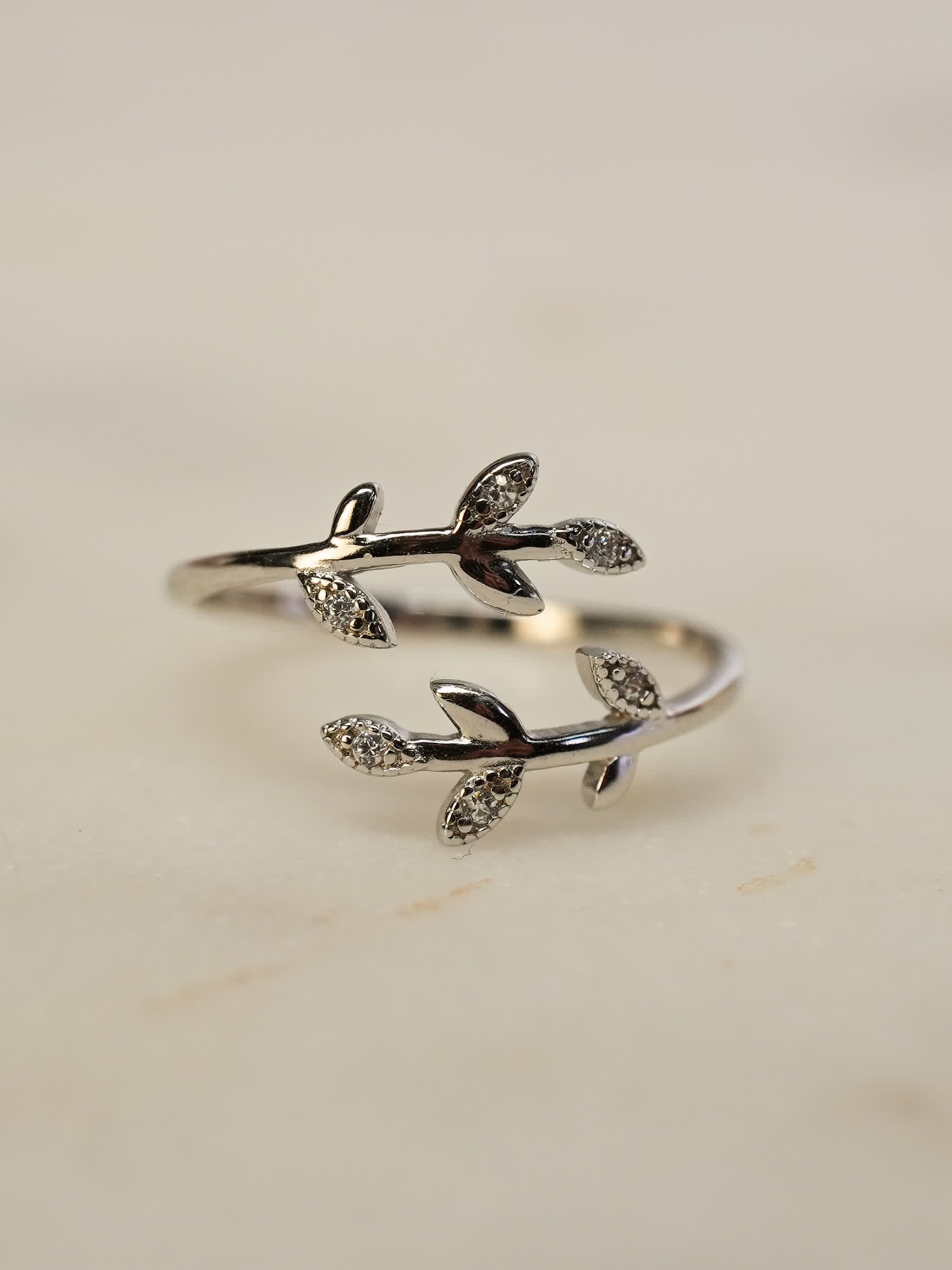 Delicate silver olive ring resting on white marble, with glistening zirconia leaves and elegant curves.