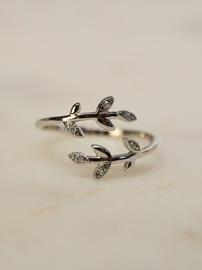 Delicate silver olive ring resting on white marble, with glistening zirconia leaves and elegant curves.
