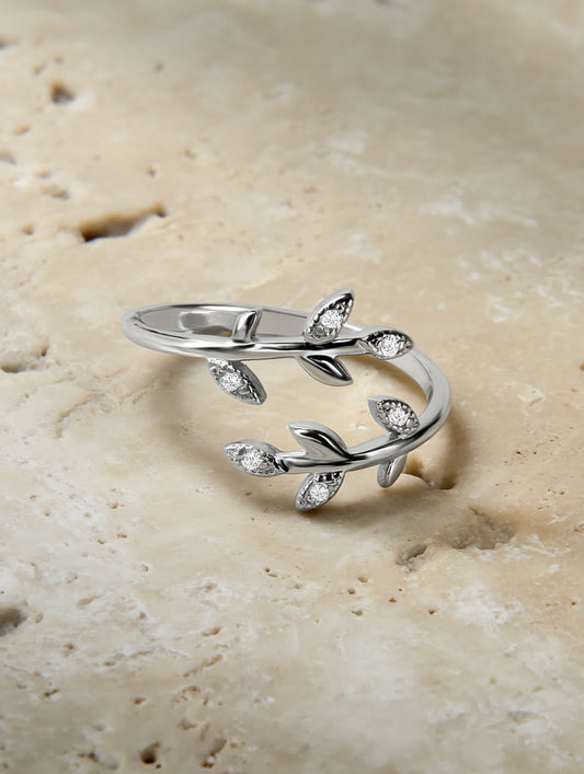 Olive leaf silver ring placed on a natural travertine slab, showcasing its organic shape and shimmering stones.