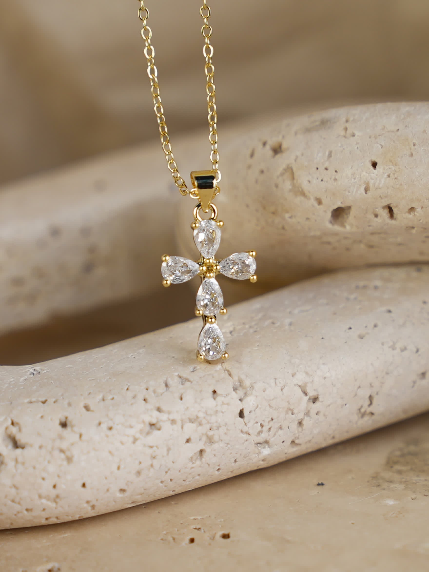 Delicate marquise and pear-cut crystal cross necklace styled on natural stone background