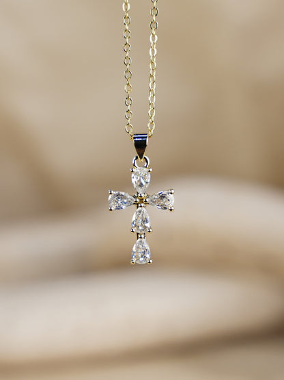 Close-up of Purelight Teardrop Crystal Cross Necklace on gold chain, displayed against soft beige background