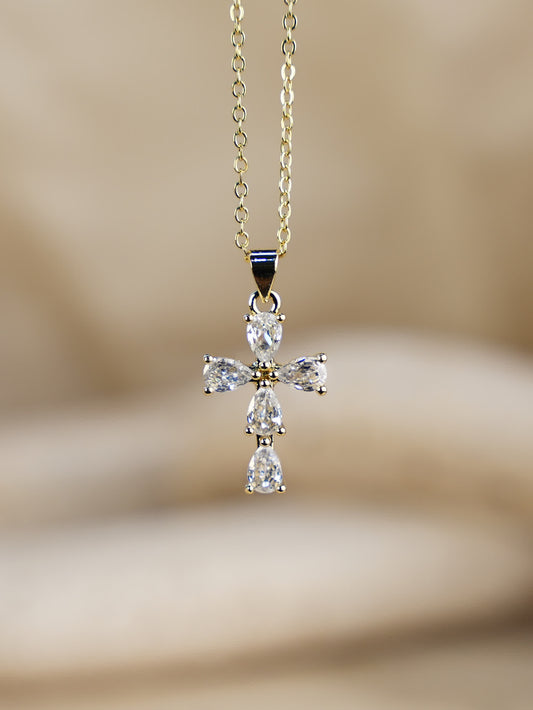 Close-up of Purelight Teardrop Crystal Cross Necklace on gold chain, displayed against soft beige background
