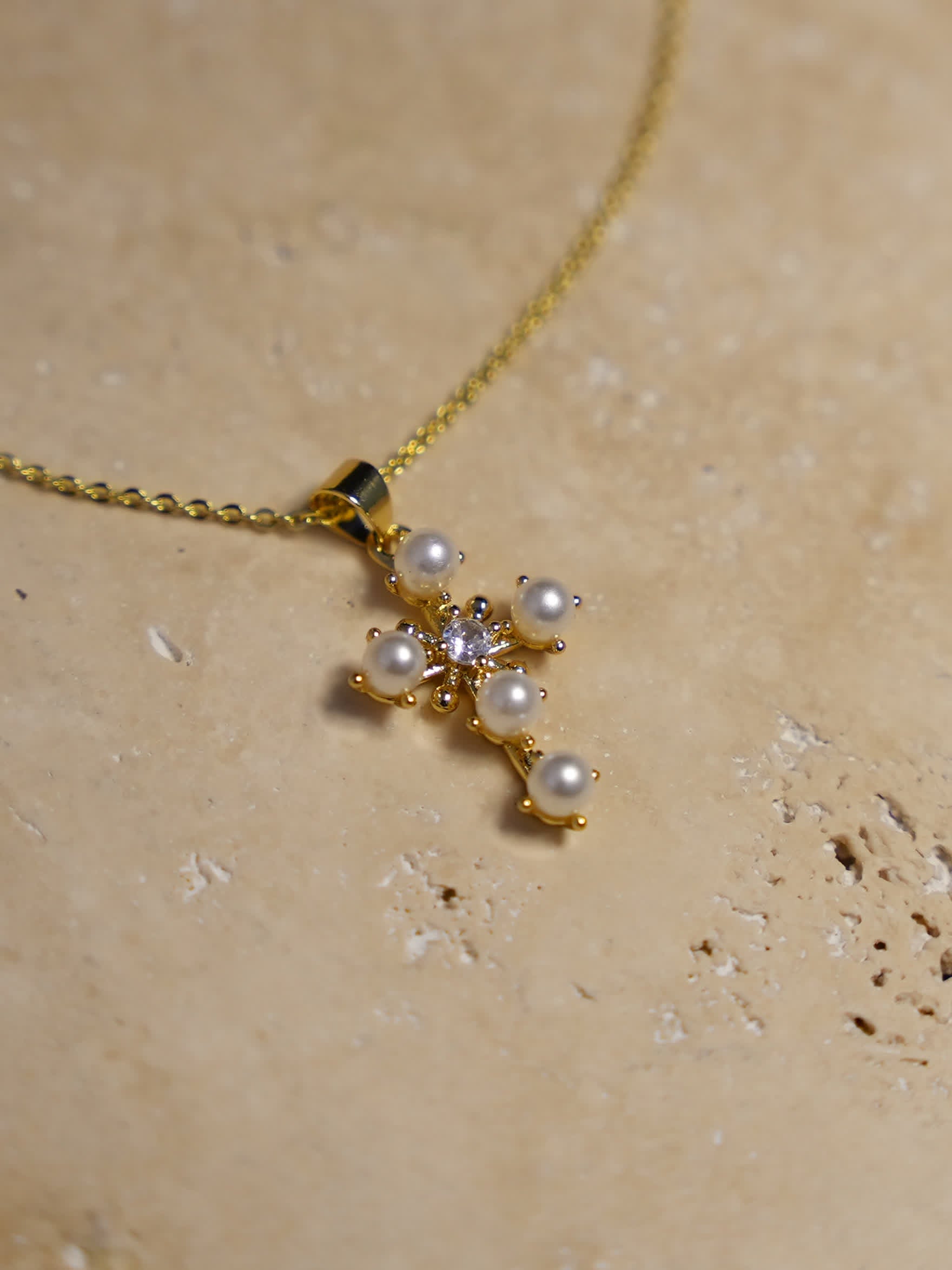 Mother of pearl floral cross necklace laid on stone surface with soft shadows