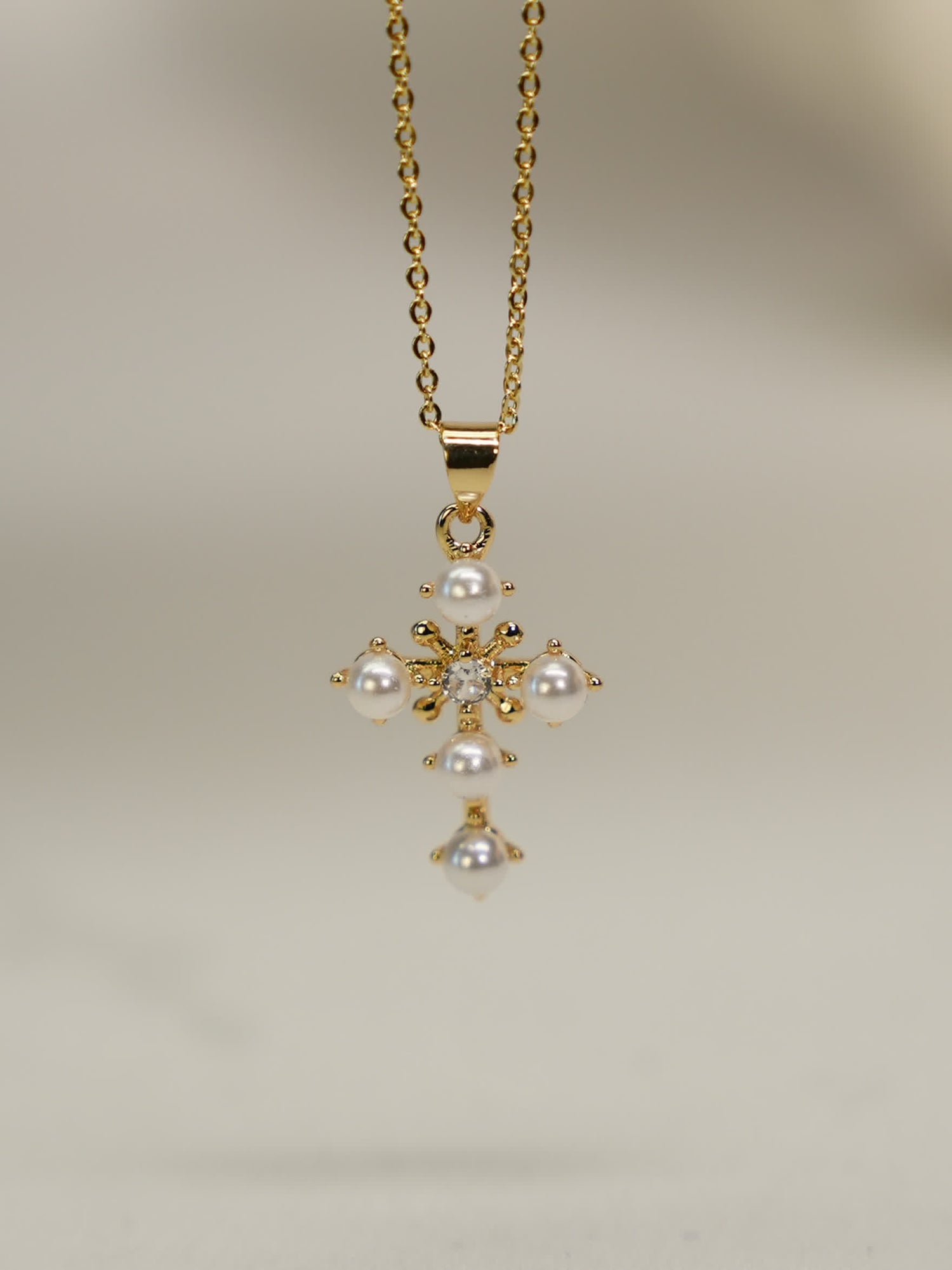 Gold floral cross pendant with resin pearls and crystal center on white background
