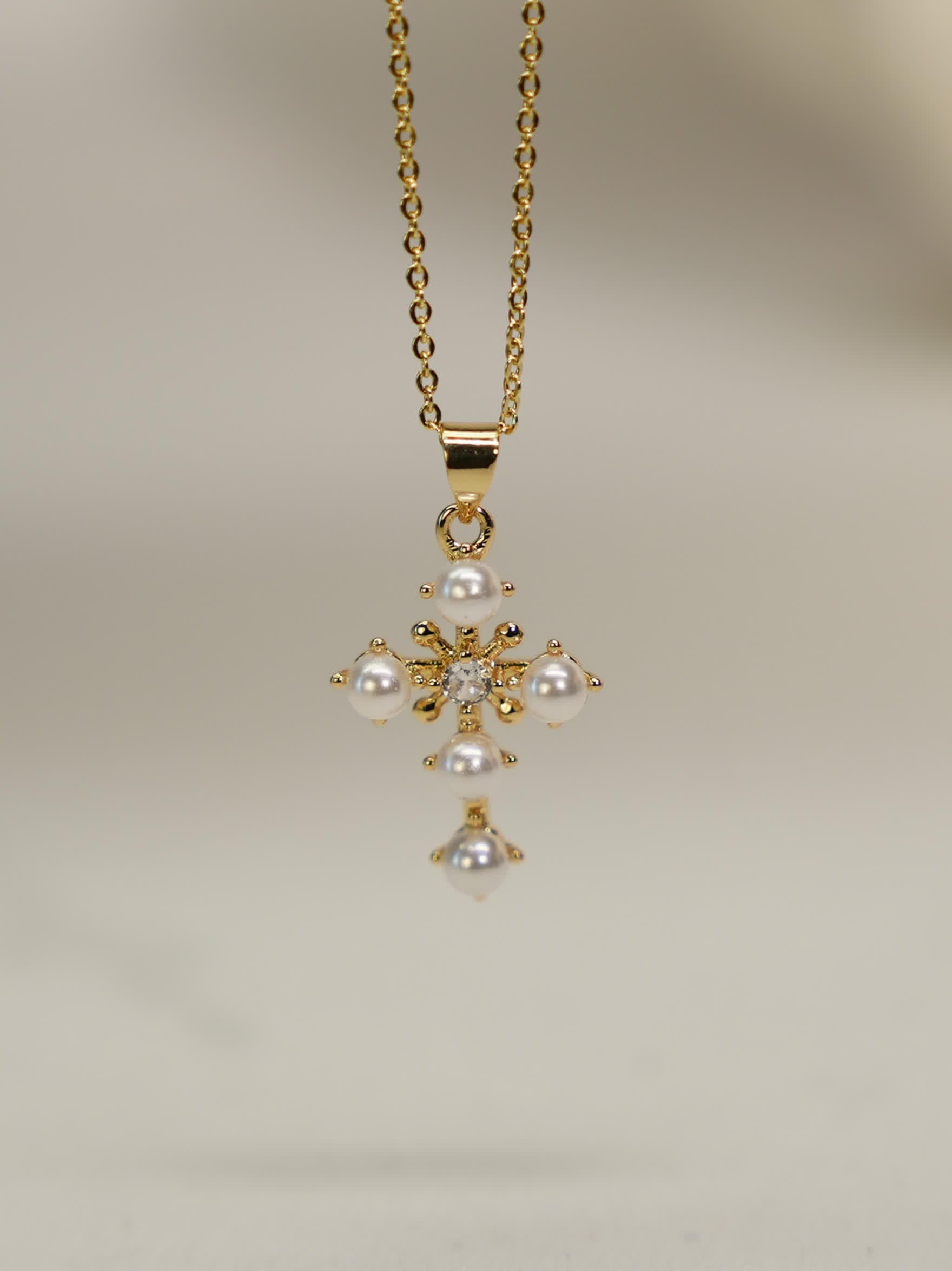 Gold floral cross pendant with resin pearls and crystal center on white background
