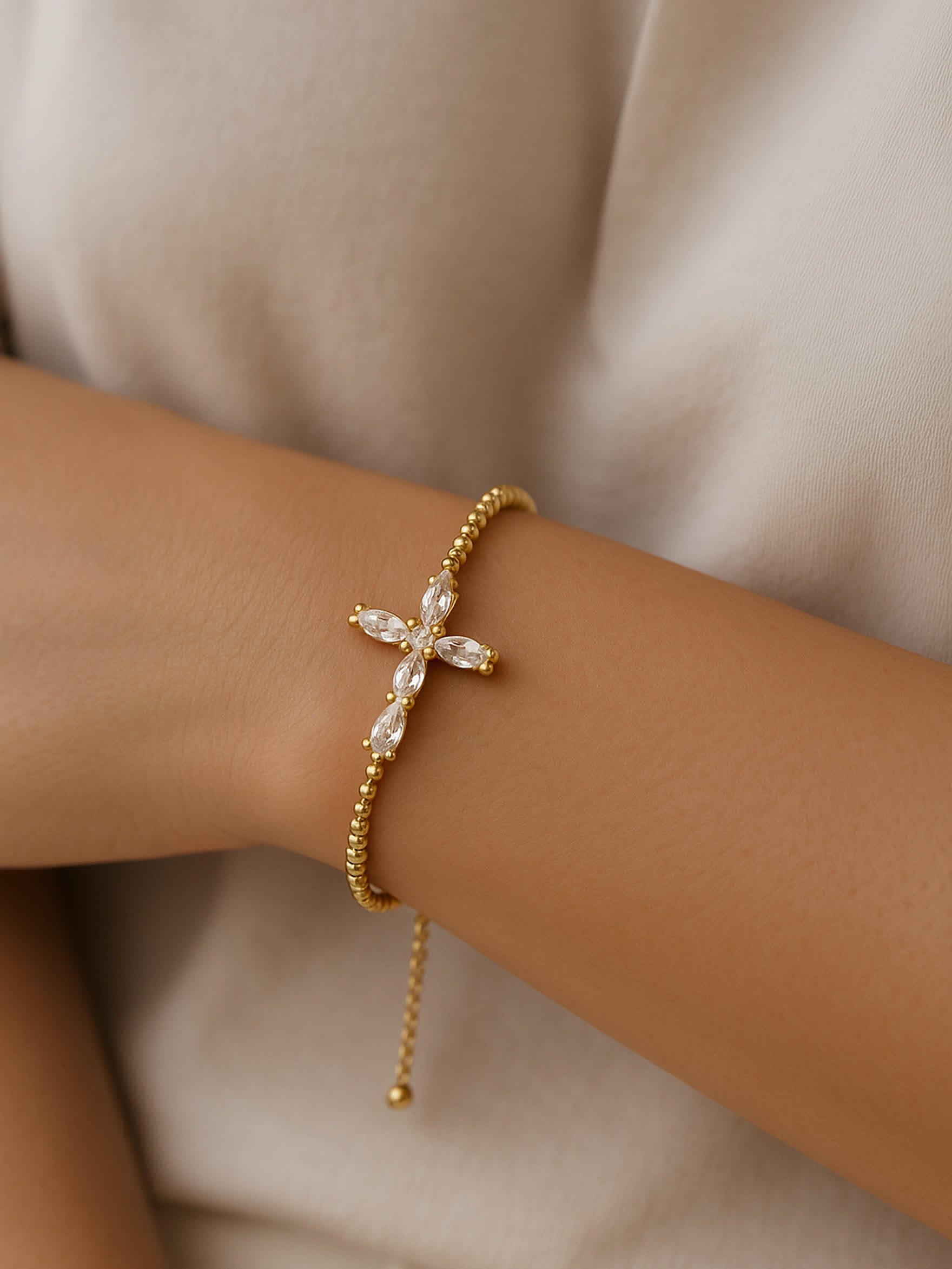 Lifestyle photo of the Radiant Mercy Gold Cross Bracelet worn on a woman's wrist, capturing the graceful drape and refined sparkle of the adjustable gold bracelet.
