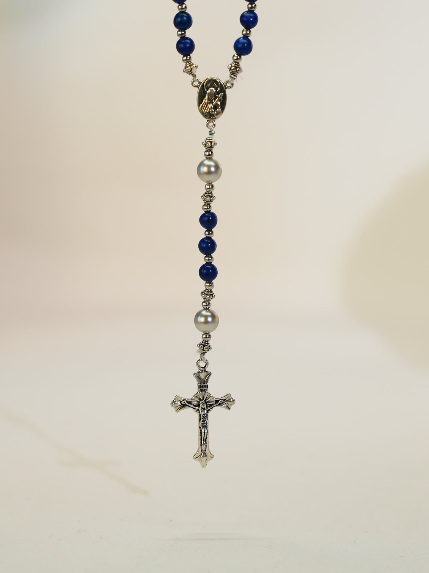 black lava rosary necklace with silver cross on neutral background