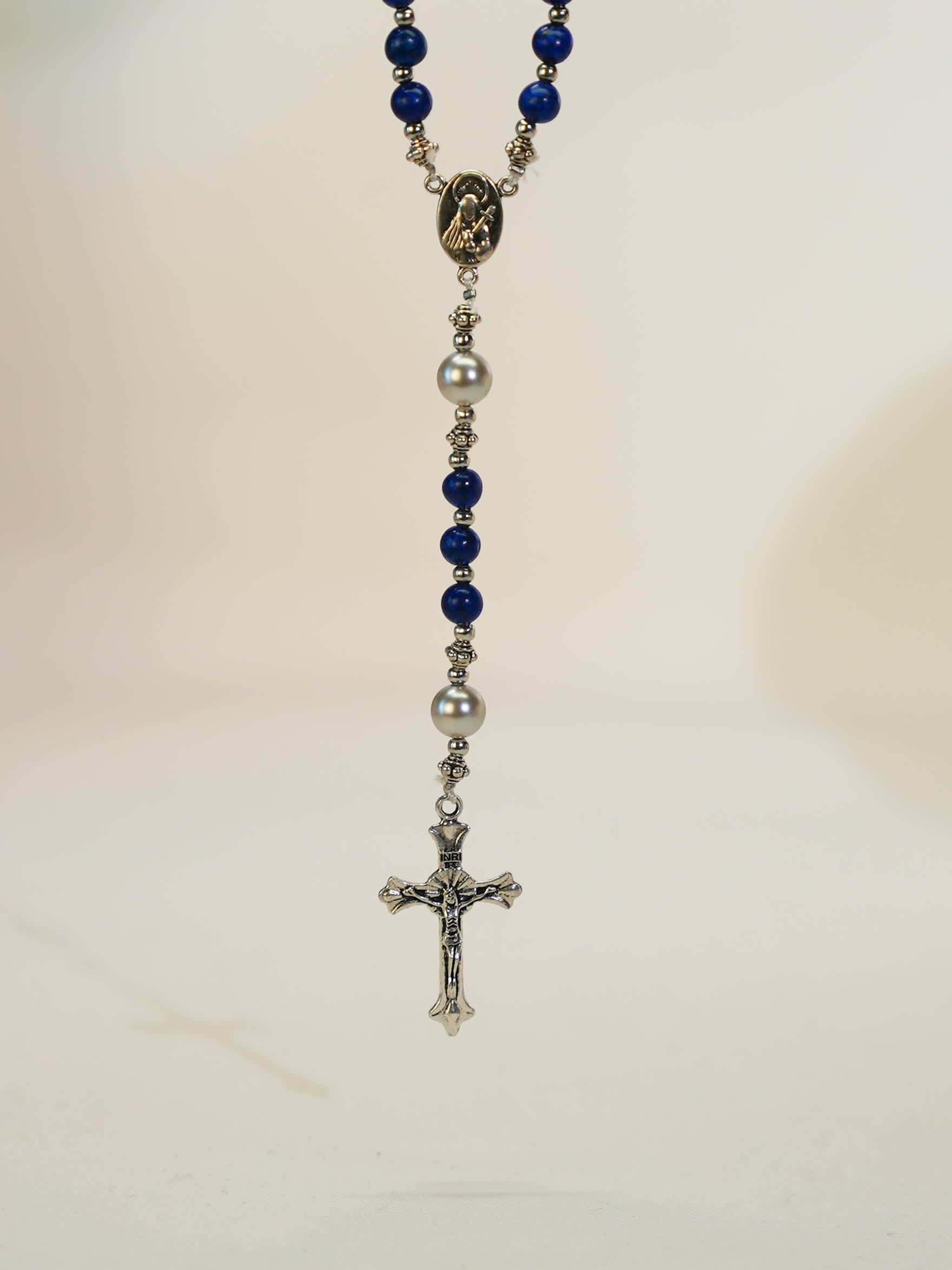 black lava rosary necklace with silver cross on neutral background