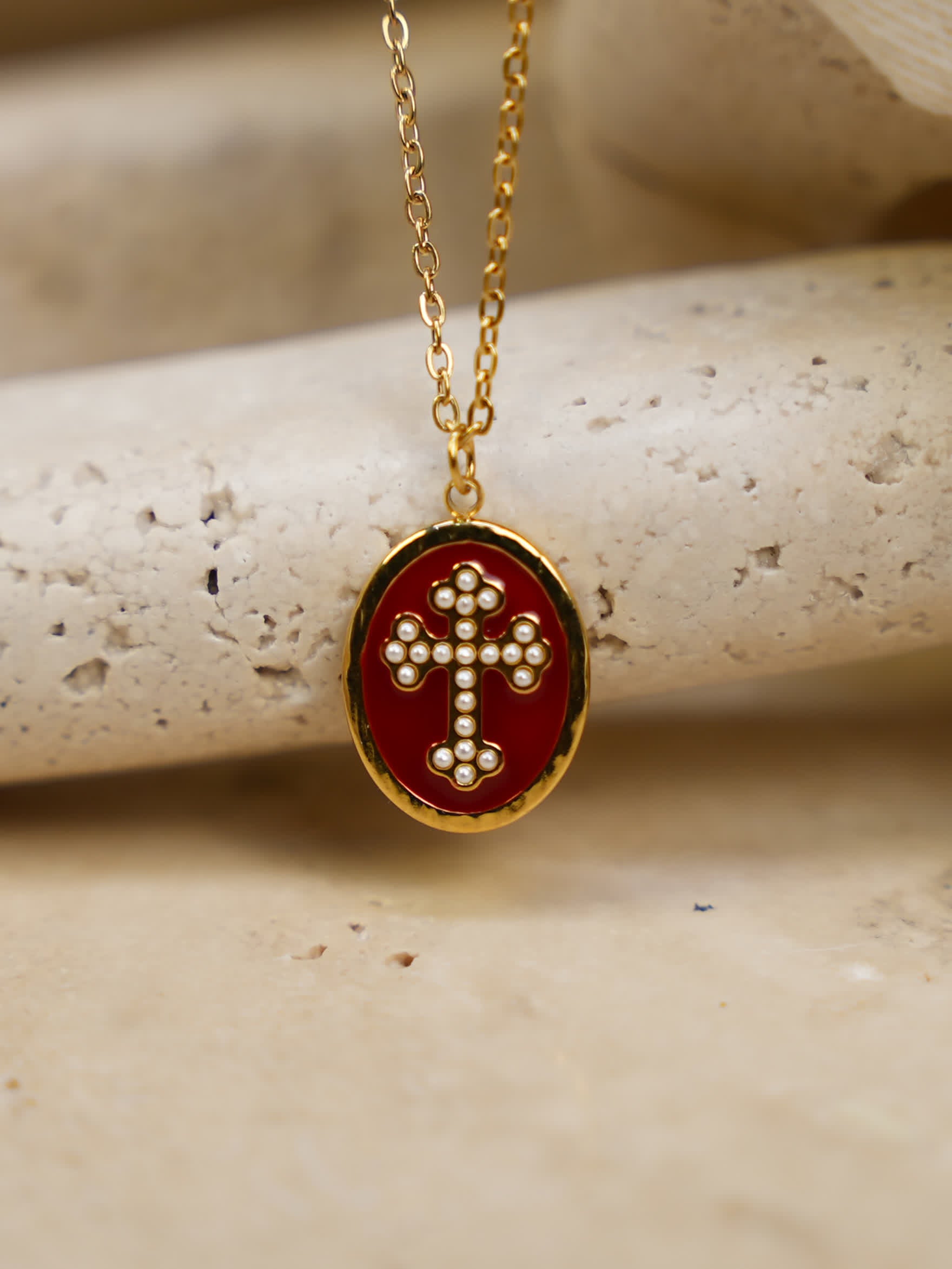 Close-up of red enamel cross necklace resting on natural travertine slab